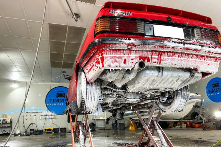 Undercarriage of a vehicle being washed, with water and cleaning equipment visible