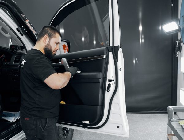 Interior door panel of a vehicle being cleaned with a cloth, showing detailed attention to the surface.