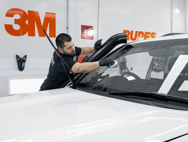 Car windscreen being cleaned with a cloth, showing the process of removing smudges and streaks.