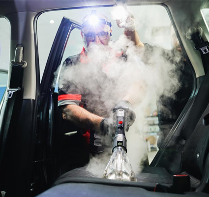 Seats of a vehicle being steam cleaned, with steam visibly lifting dirt and grime.