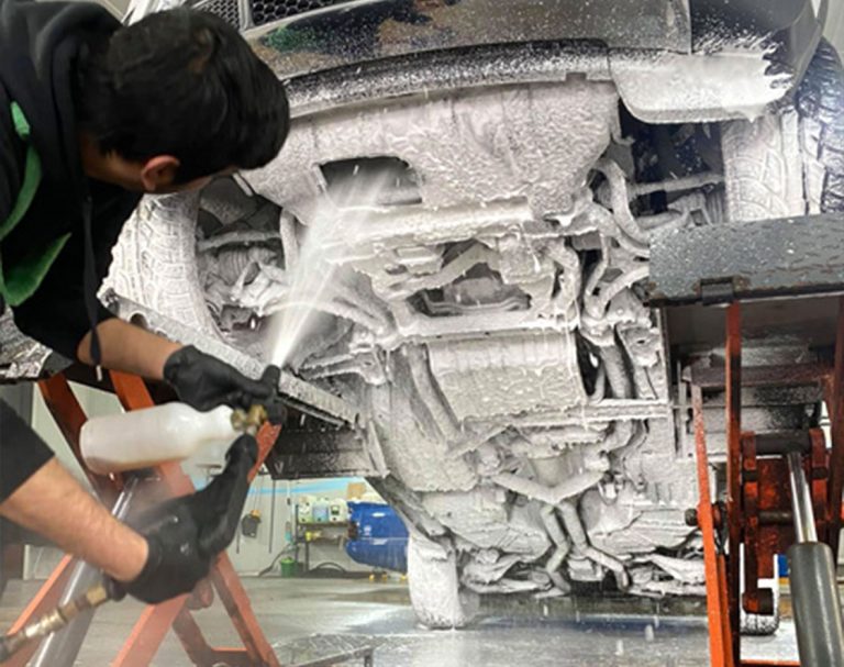 Undercarriage of a vehicle being washed, with water and cleaning equipment visible