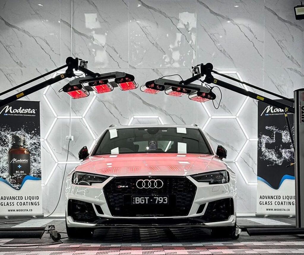 Audi RS4 positioned under heat lamps to cure the ceramic coating, with the car’s exterior being treated by the heat