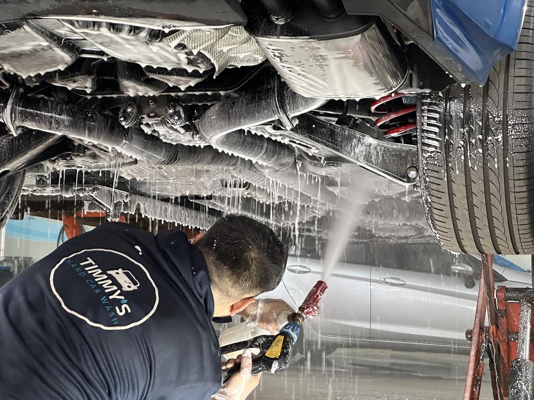 Undercarriage of a vehicle being washed, with water and cleaning equipment visible.