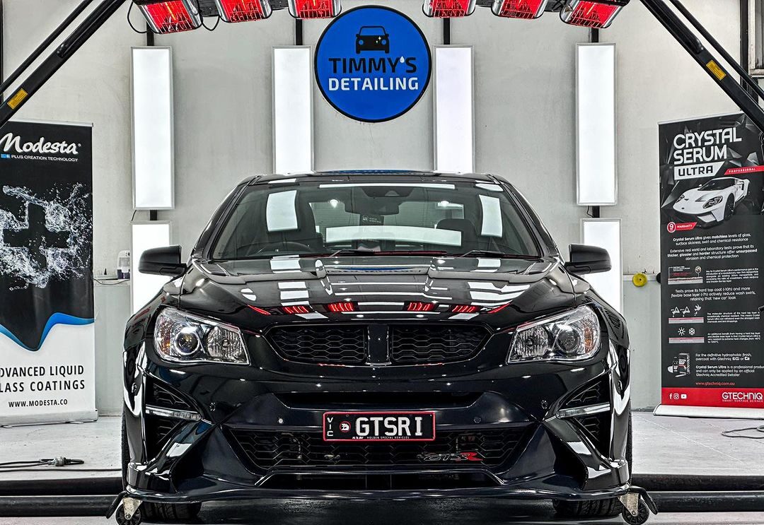 Holden sports car positioned under heat lamps to cure the ceramic coating, with the car’s exterior being treated.