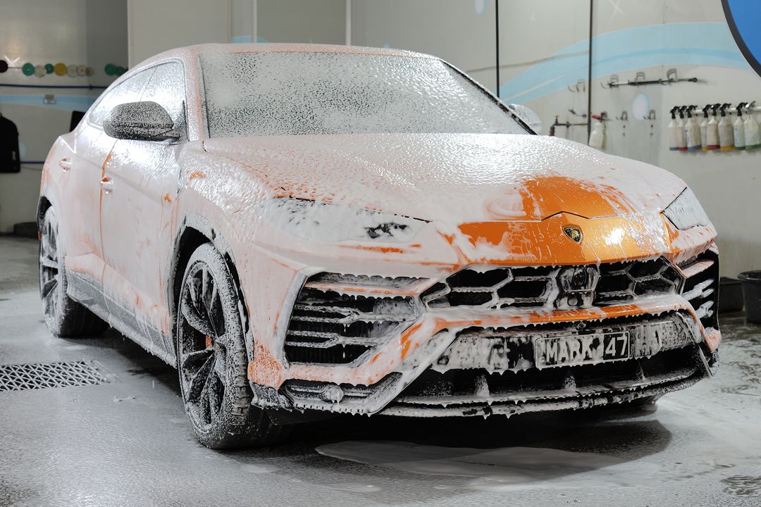 Orange Lamborghini Urus covered in foam during a wash process.