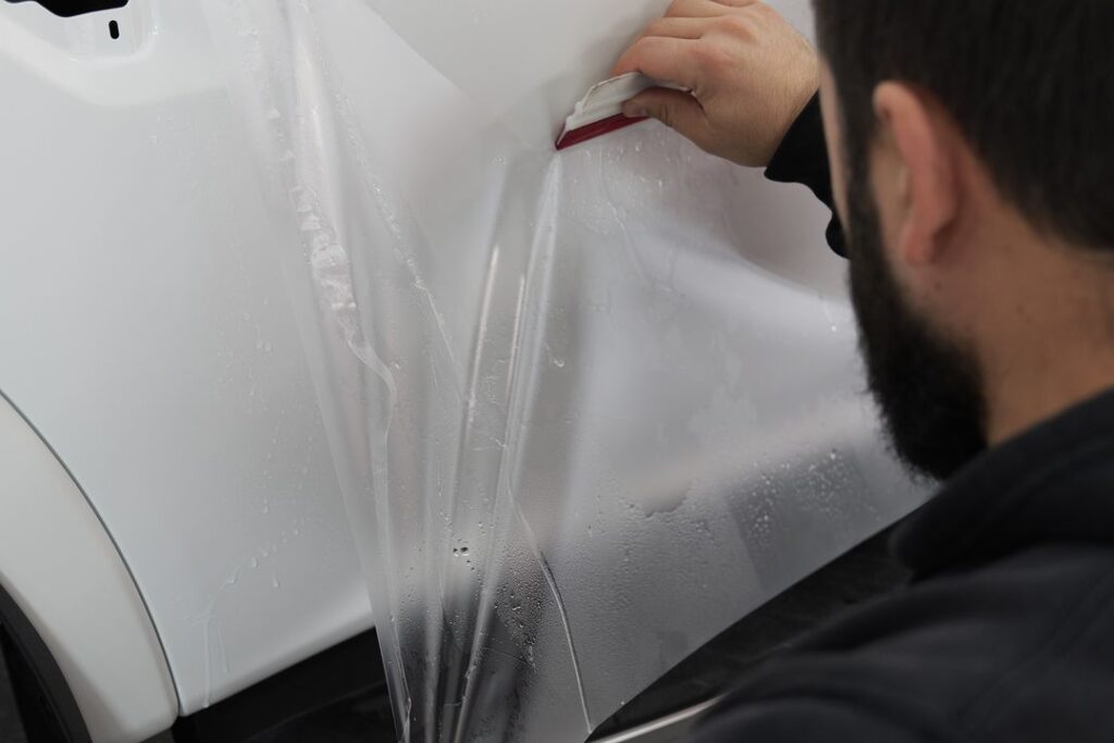 Application of Paint Protection Film (PPF) on a vehicle’s exterior, with film being carefully applied to the surface.